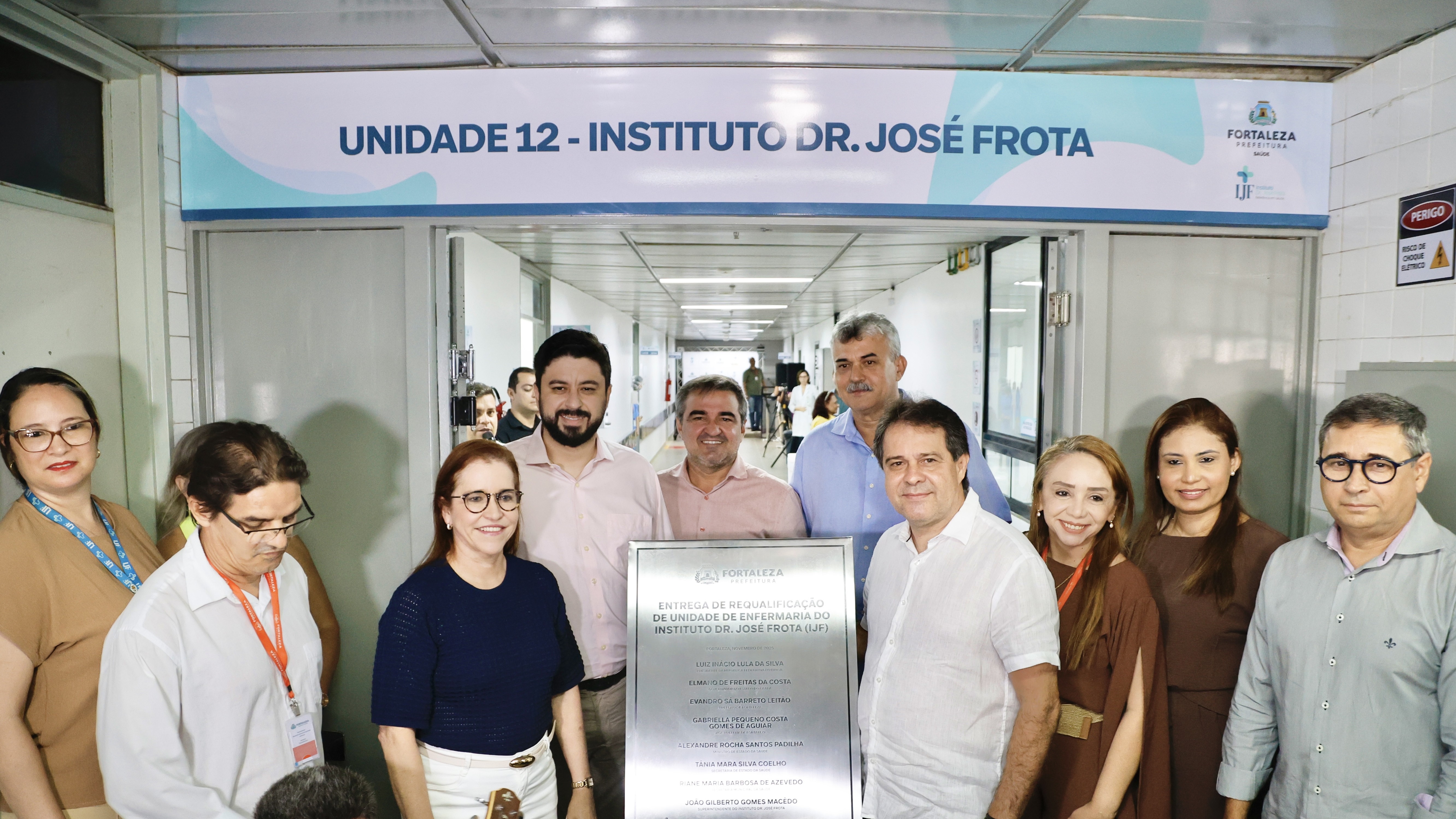 grupo de pessoas posa junto à placa de inauguração da ala do IJF